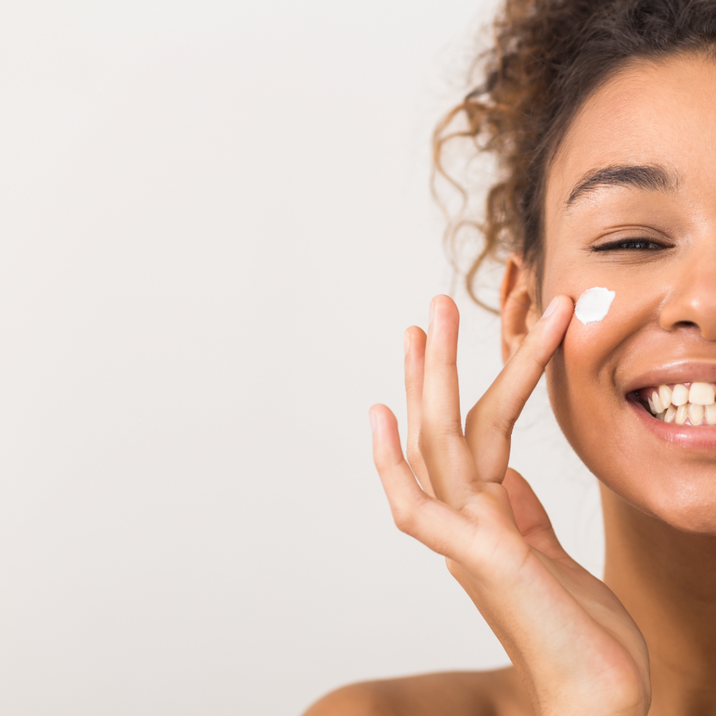 Close-up of a smiling woman applying face cream to her cheek with her finger. Autumn reset.
