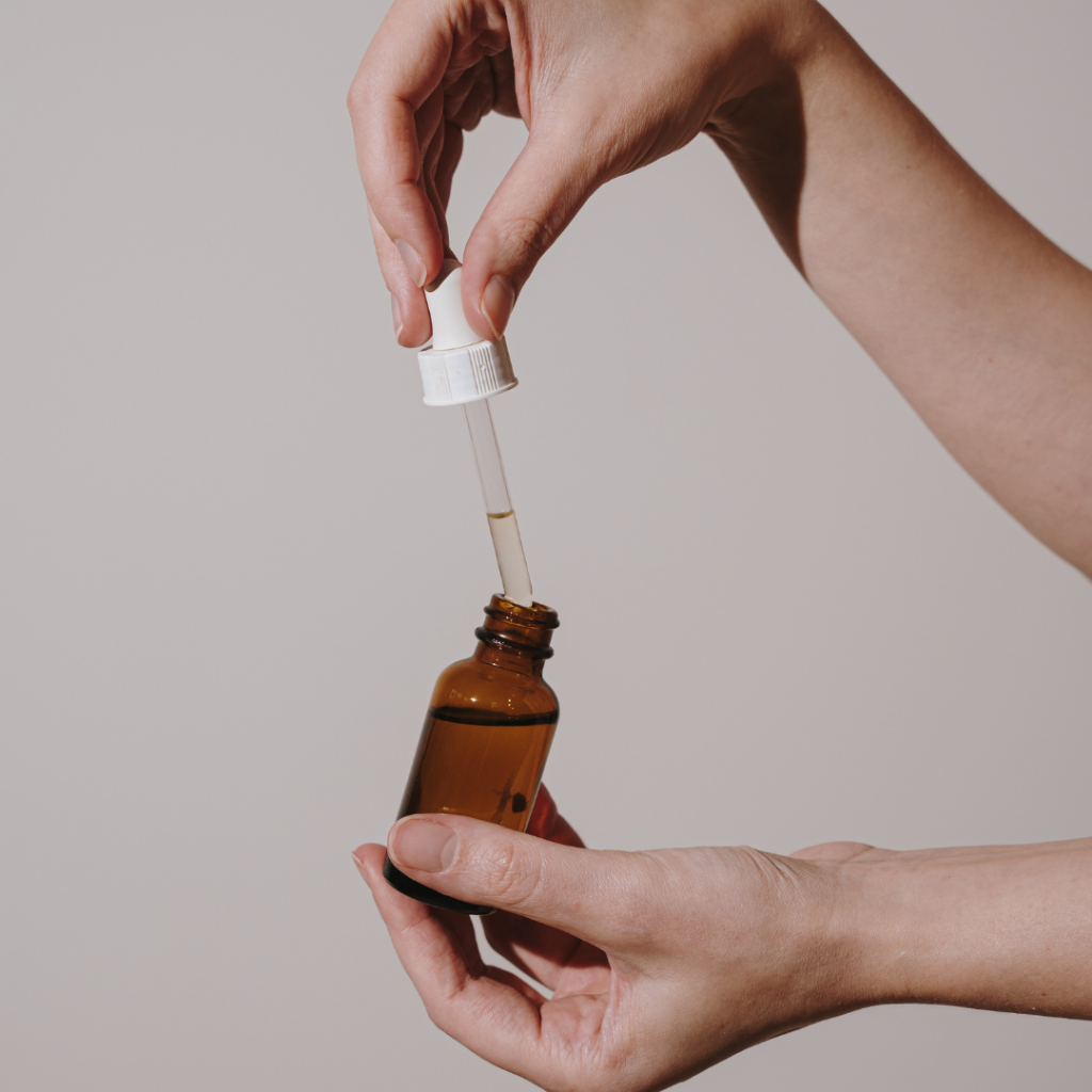 Close-up of hands holding a brown glass dropper bottle, with the dropper being removed and containing a small amount of liquid. Autumn reset.