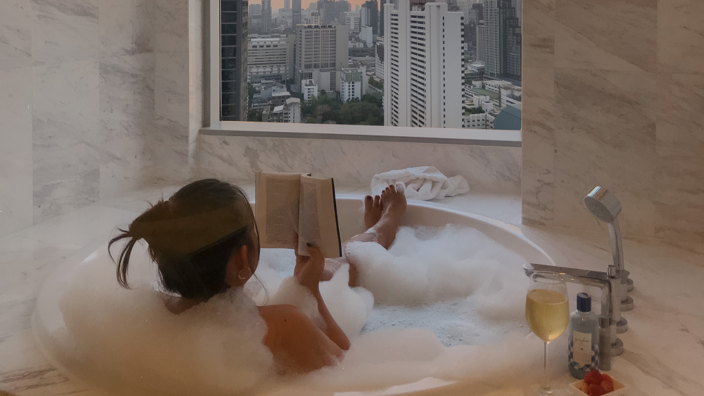Woman in a bubble bath reading a book in front of a window with buildings in the background.

Lessons About Self-Love